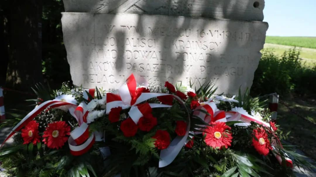 Pomnik ofiar zbrodni UPA z 1944 roku w Bełżcu, przed którym ułożono wieńce i kwiaty ozdobione biało-czerwonymi wstążkami – symbol pamięci i hołdu dla pomordowanych.