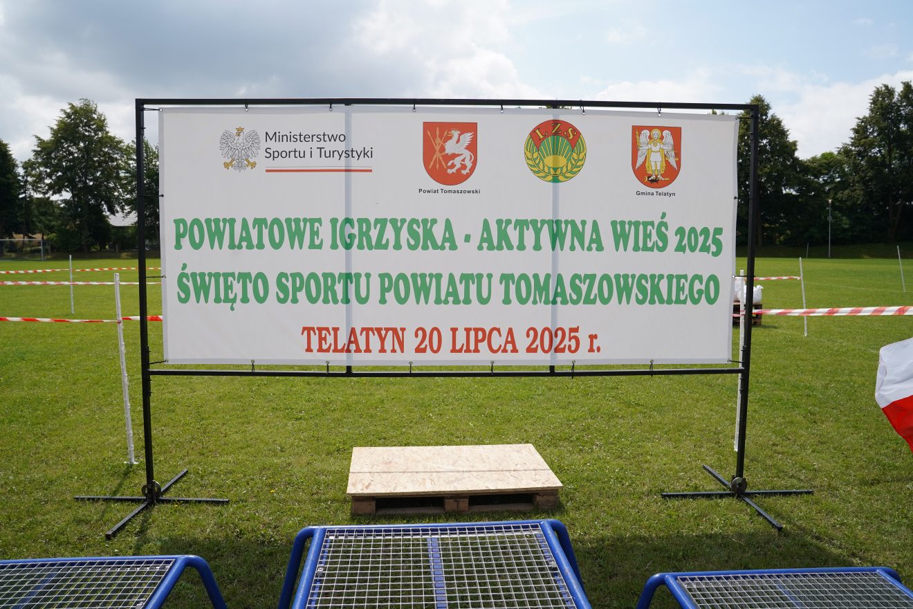 Zdjęcie przedstawia baner promujący Powiatowe Igrzyska - Aktywna Wieś Święto Sportu Powiatu Tomaszowskiego. Znajdują się też na nim logo Ministerstwa Sportu i Turystyki, Powiatu Tomaszowskiego, LZS i Gminy Telatyn.