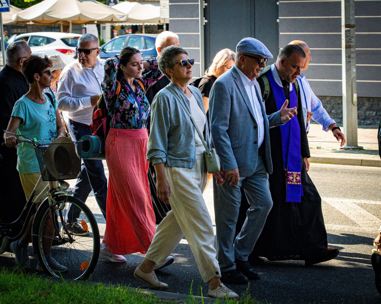 Młodzież i starsi uczestnicy pielgrzymki idą razem. W tle widoczny fragment miasta.