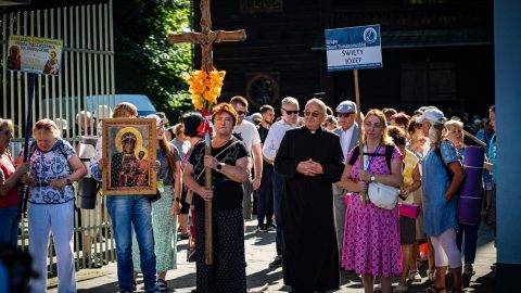 Grupa pielgrzymów wyrusza pieszo z Tomaszowa Lubelskiego. Na czele niesiony jest krzyż. W tle kościół.