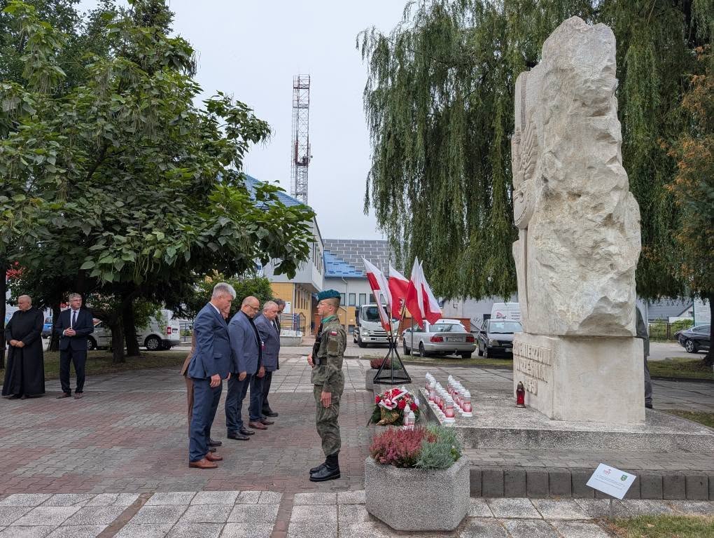 Pomnik „Żołnierzom Września 1939 r.”, przed którym stoi warta honorowa zwrócona tyłem do pomnika. U jego stóp leżą znicze, a uczestnicy uroczystości składają hołd poległym obrońcom Ojczyzny. W tle widoczne są biało-czerwone flagi.