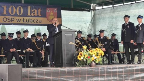 Dariusz Czop, członek Zarządu Powiatu, przemawia na jubileuszu 100-lecia OSP Łubcze, w tle siedzą strażacy.