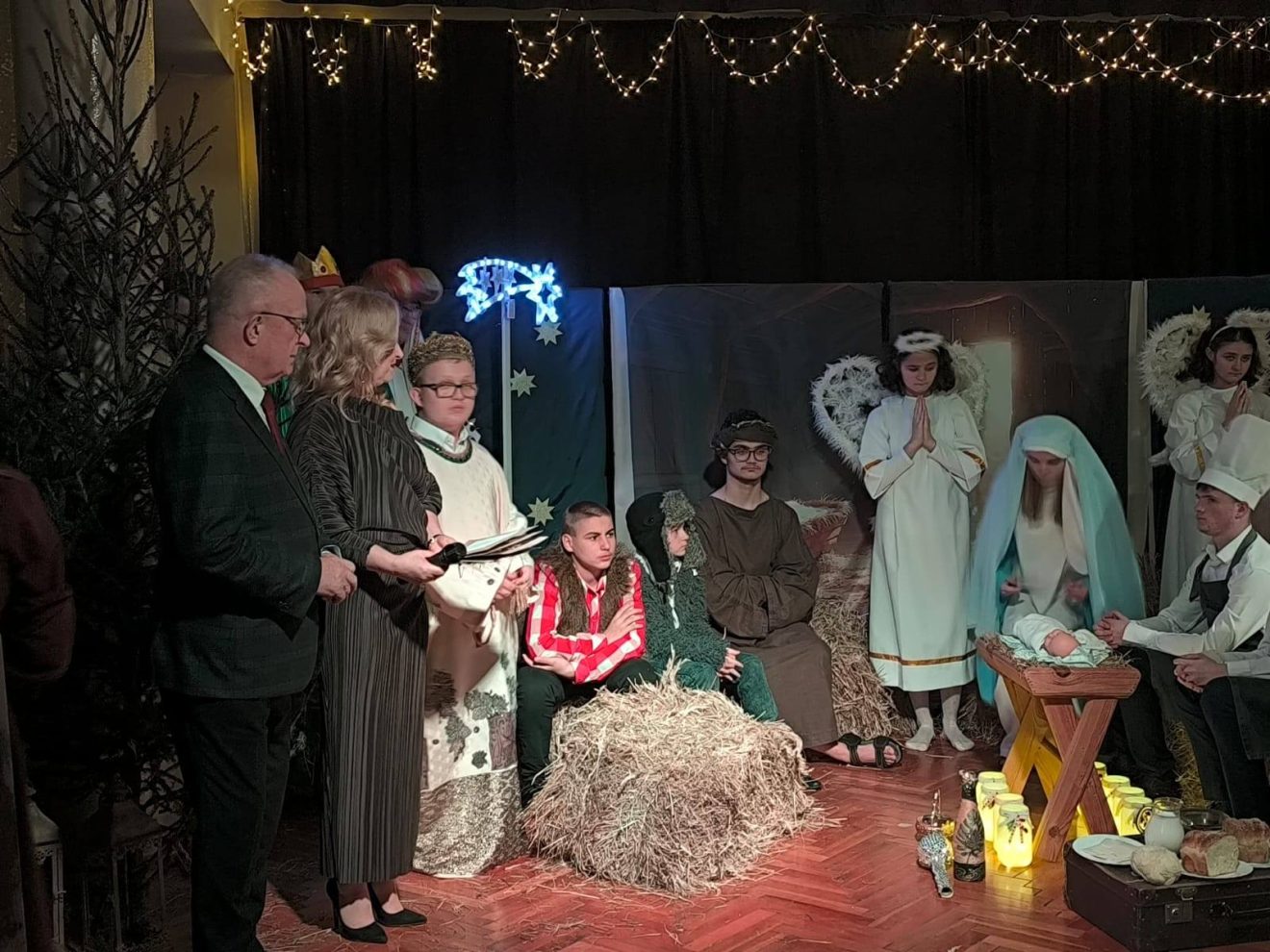 Uczniowie i zaproszeni goście podczas szkolnego Wieczoru Wigilijnego – scena jasełek z Maryją, Józefem, Dzieciątkiem Jezus i aniołami w świątecznej scenerii.