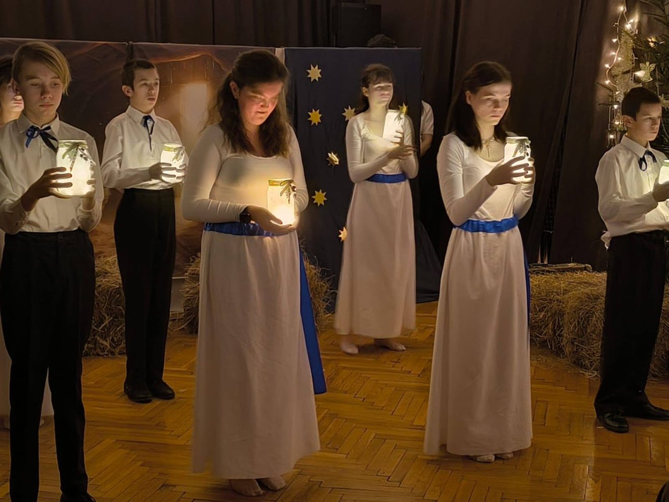 Wychowankowie trzymający lampiony podczas Wieczoru Wigilijnego, w świątecznej i nastrojowej scenerii.