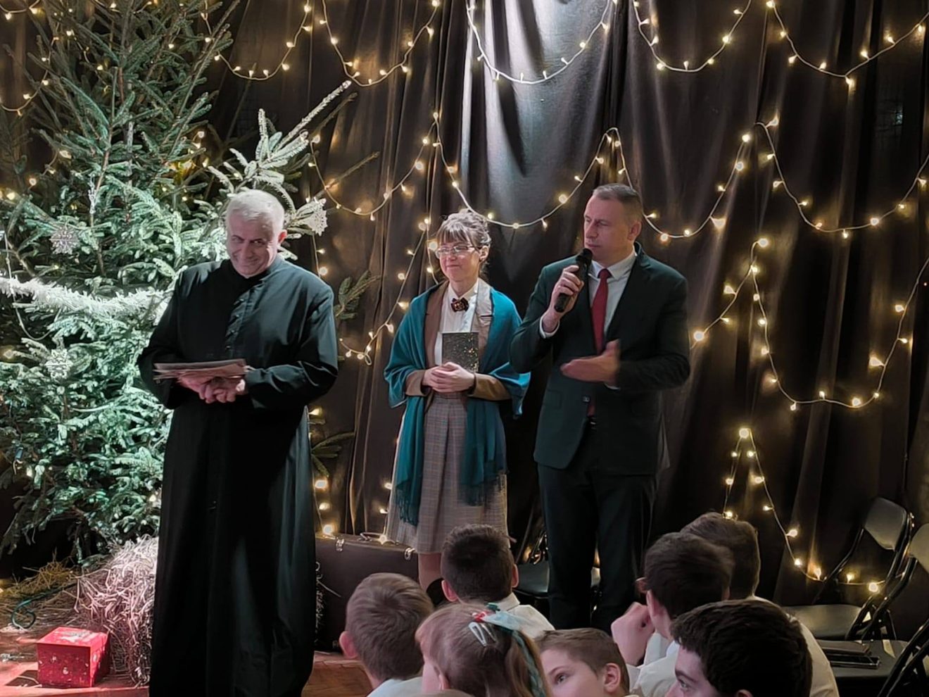 Przewodniczący Rady Powiatu przemawia podczas Wieczoru Wigilijnego, obok ksiądz oraz wychowankowie