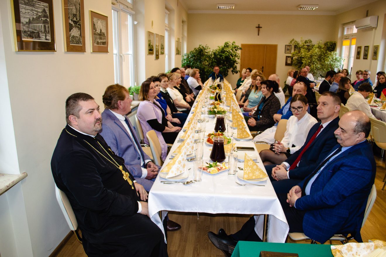Uczestnicy spotkania opłatkowego w SP ZOZ w Tomaszowie Lubelskim siedzą przy udekorowanym stole.