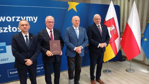 Na zdjęciu znajdują się: Henryk Karwan- Starosta Tomaszowski, Wiesław Bondyra - Dyrektor Powiatowego Urzędu Pracy, Jarosław Stawiarski - Marszałek Województwa Lubelskiego, na tle niebieskiej ścianki informacyjnej , a po prawej stronie zdjęcia znajdują się flagi: polska i urzędu marszałkowskiego.