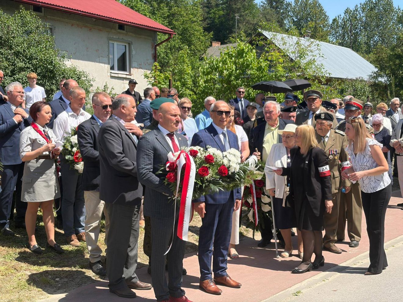 Delegacje i mieszkańcy gromadzą się z wieńcami przed złożeniem kwiatów pod pomnikiem.