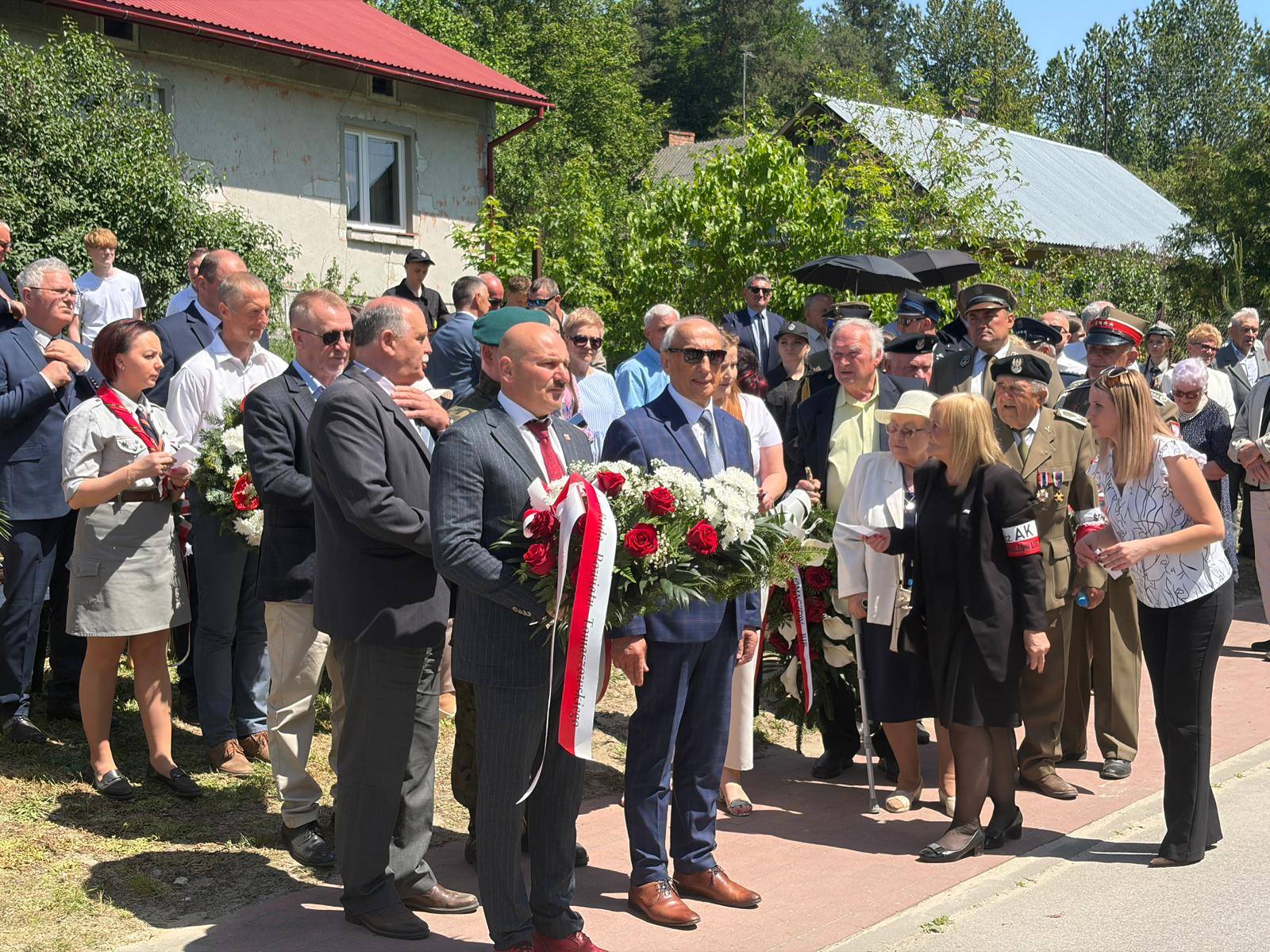 Delegacje i mieszkańcy gromadzą się z wieńcami przed złożeniem kwiatów pod pomnikiem.
