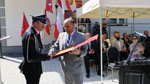 Przedstawiciel samorządu wręcza strażakowi pamiątkowy grawerton podczas jubileuszu OSP.
