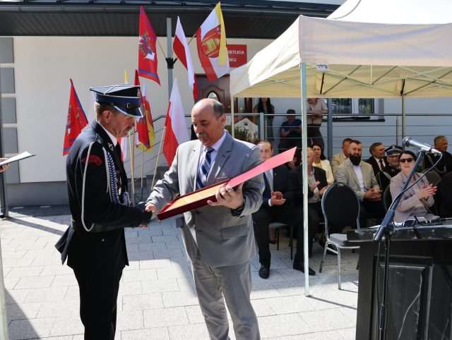 Przedstawiciel samorządu wręcza strażakowi pamiątkowy grawerton podczas jubileuszu OSP.