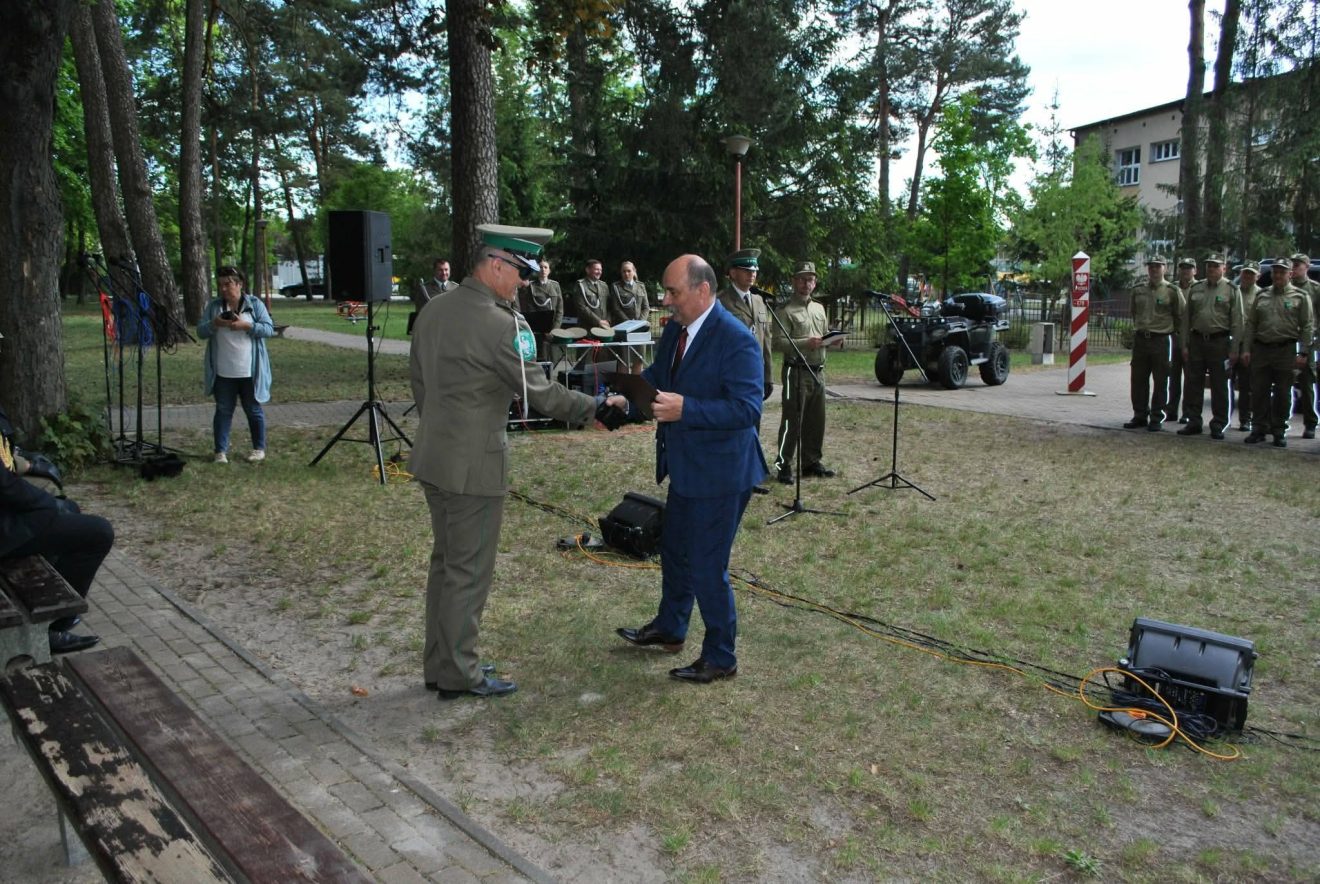 Przedstawiciel Powiatu Tomaszowskiego wręcza upominek funkcjonariuszowi Straży Granicznej podczas uroczystości w parku.