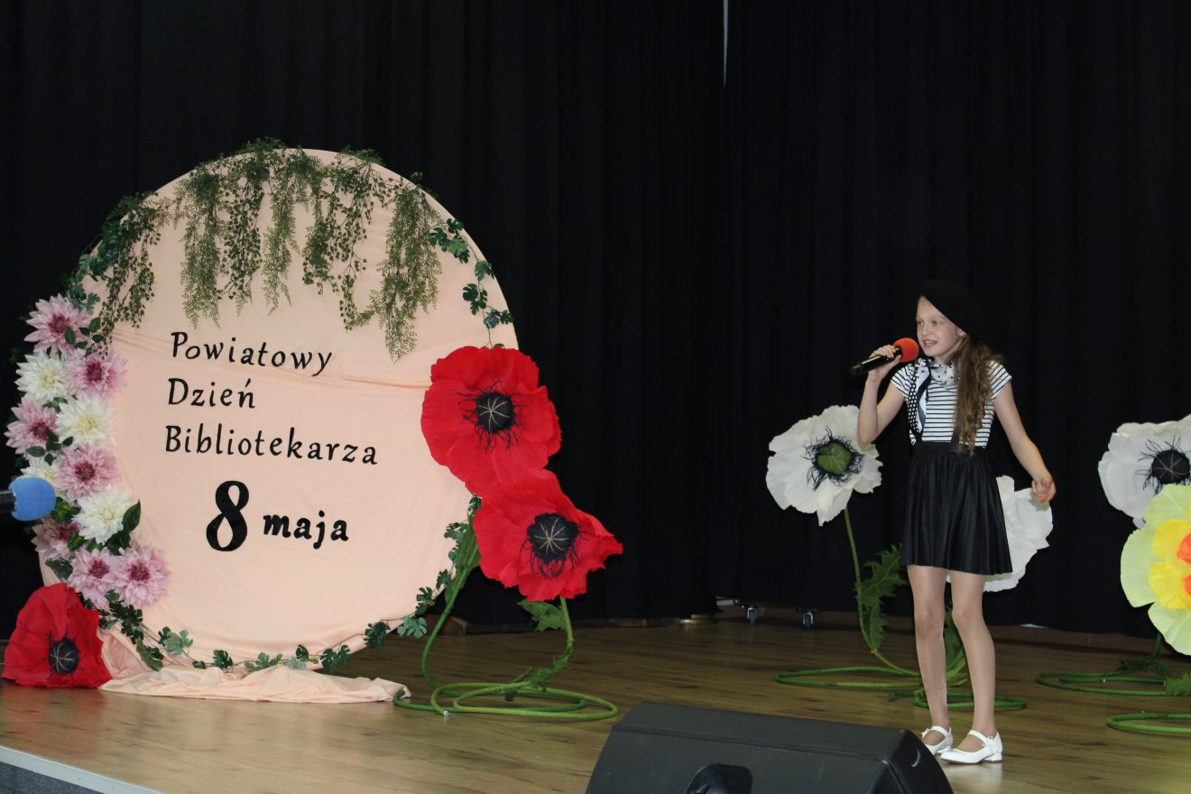 Dziewczynka śpiewa na scenie podczas Powiatowego Dnia Bibliotekarza.