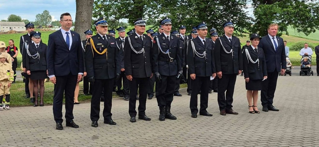 Strażacy i uczestnicy obchodów stoją w szeregu podczas oficjalnej części jubileuszu OSP Nowosiółki.
