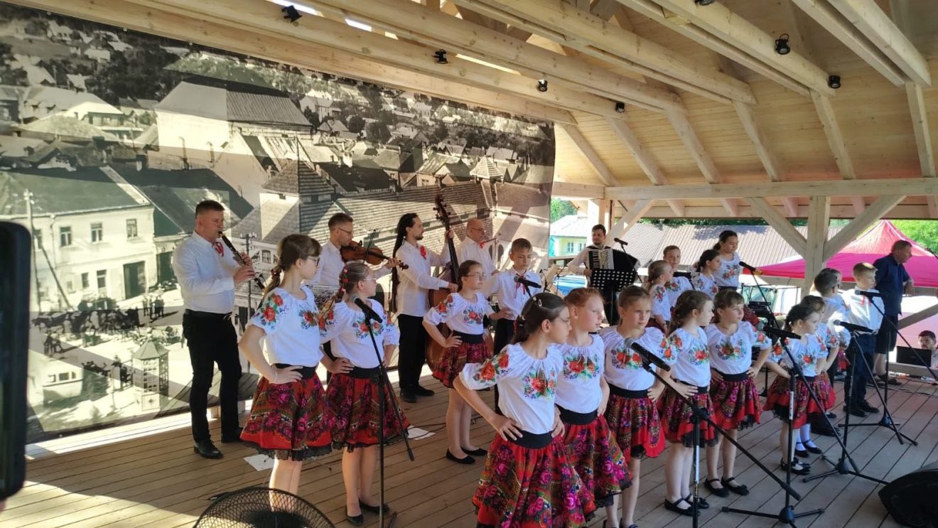 Dziecięcy zespół folklorystyczny występuje na scenie w tradycyjnych strojach ludowych.