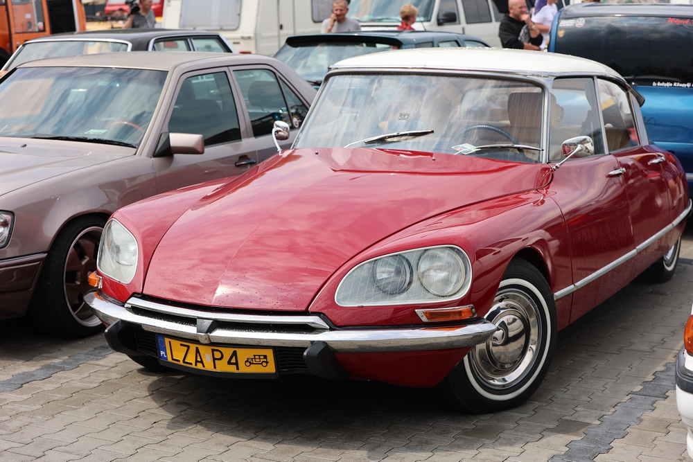 Czerwony Citroën DS zaparkowany wśród zabytkowych samochodów.