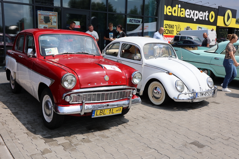 Czerwony Moskwicz i biały Volkswagen Garbus zaparkowane obok siebie podczas zlotu.