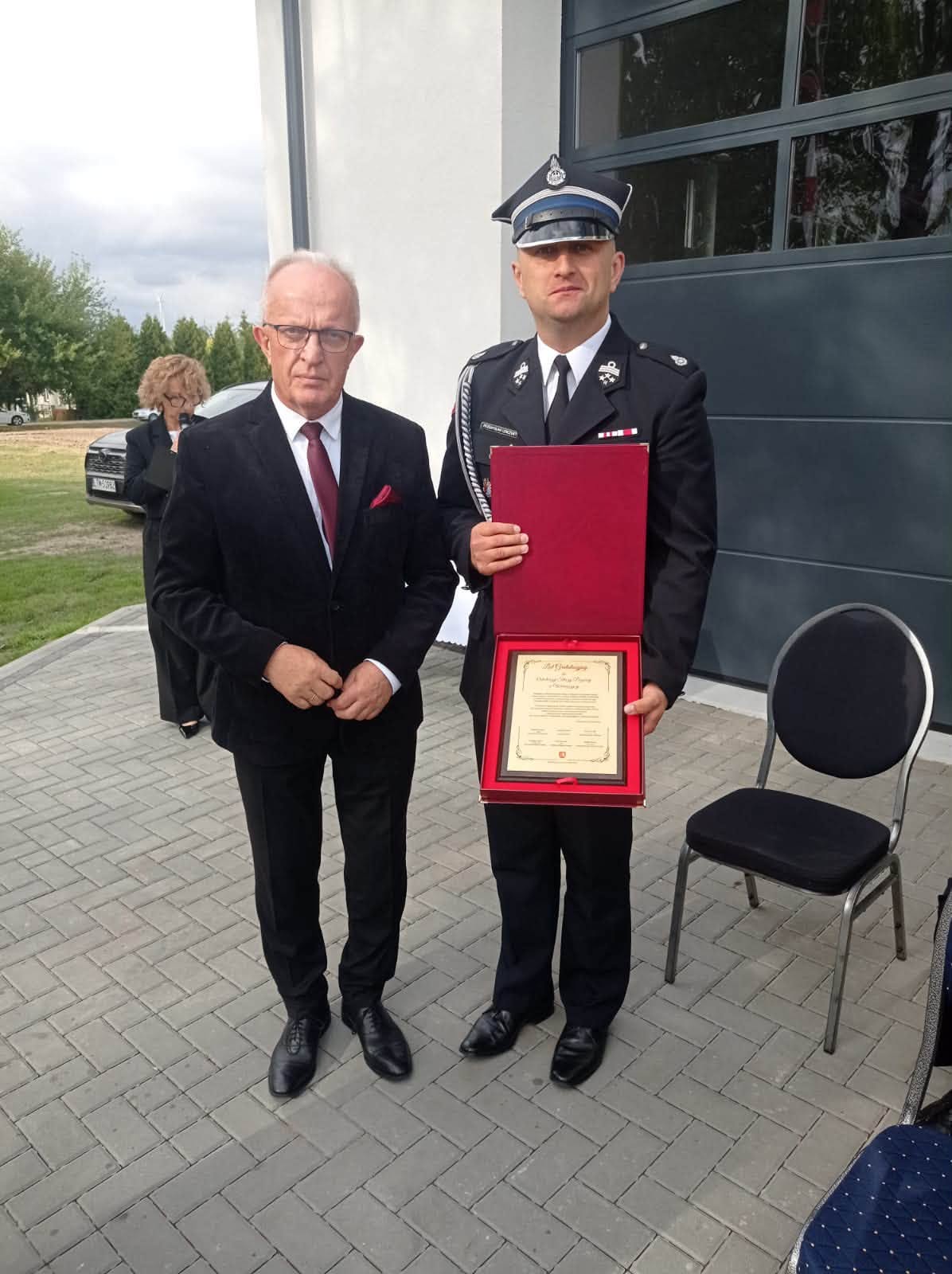 Starosta Tomaszowski i przedstawiciel OSP pozują do zdjęcia z pamiątkowym wyróżnieniem wręczonym jednostce.
