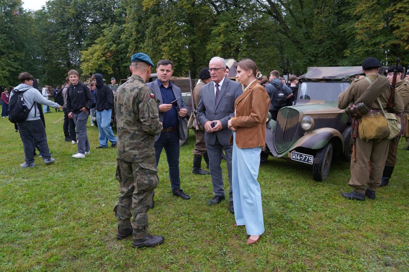 Starosta Tomaszowski Henryk Karwan podczas rozmowy z żołnierzem w otoczeniu historycznych pojazdów wojskowych. W tle młodzież uczestnicząca w wydarzeniu „Wojenne Drogi”.