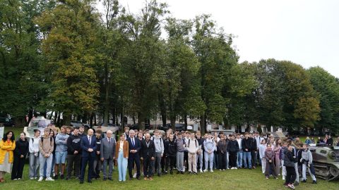 Grupowe zdjęcie młodzieży i uczestników wydarzenia „Wojenne Drogi” na tle historycznych pojazdów wojskowych.