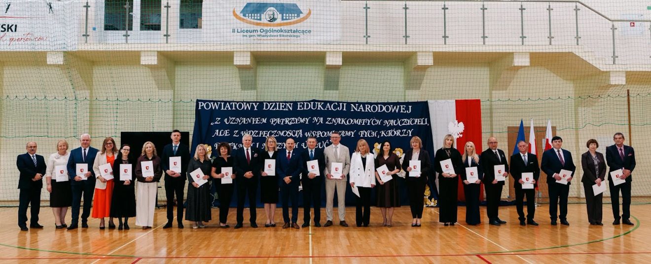 Grupa nauczycieli i pracowników oświaty pozuje do wspólnego zdjęcia, trzymając pamiątkowe dyplomy.
